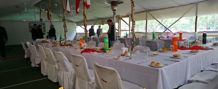 Carpa de eventos montada con mesas largas vestidas de blanco.