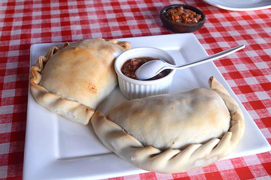 Dos empanadas de horno recién salidas, servidas con pebre sobre mantel a cuadros.