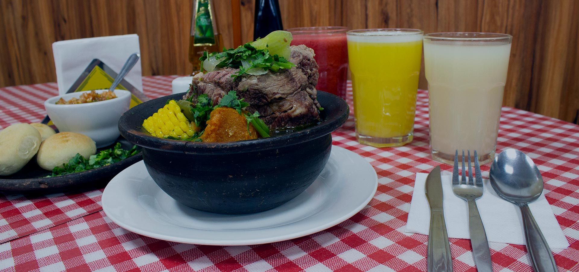 Cazuela servida en fuente de greda sobre el mantel a cuadros de Don Benito, junto a pan amasado y pebre.