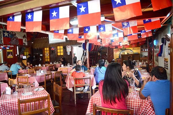 Salón del restaurant lleno de comensales, con mesas de mantel a cuadros.